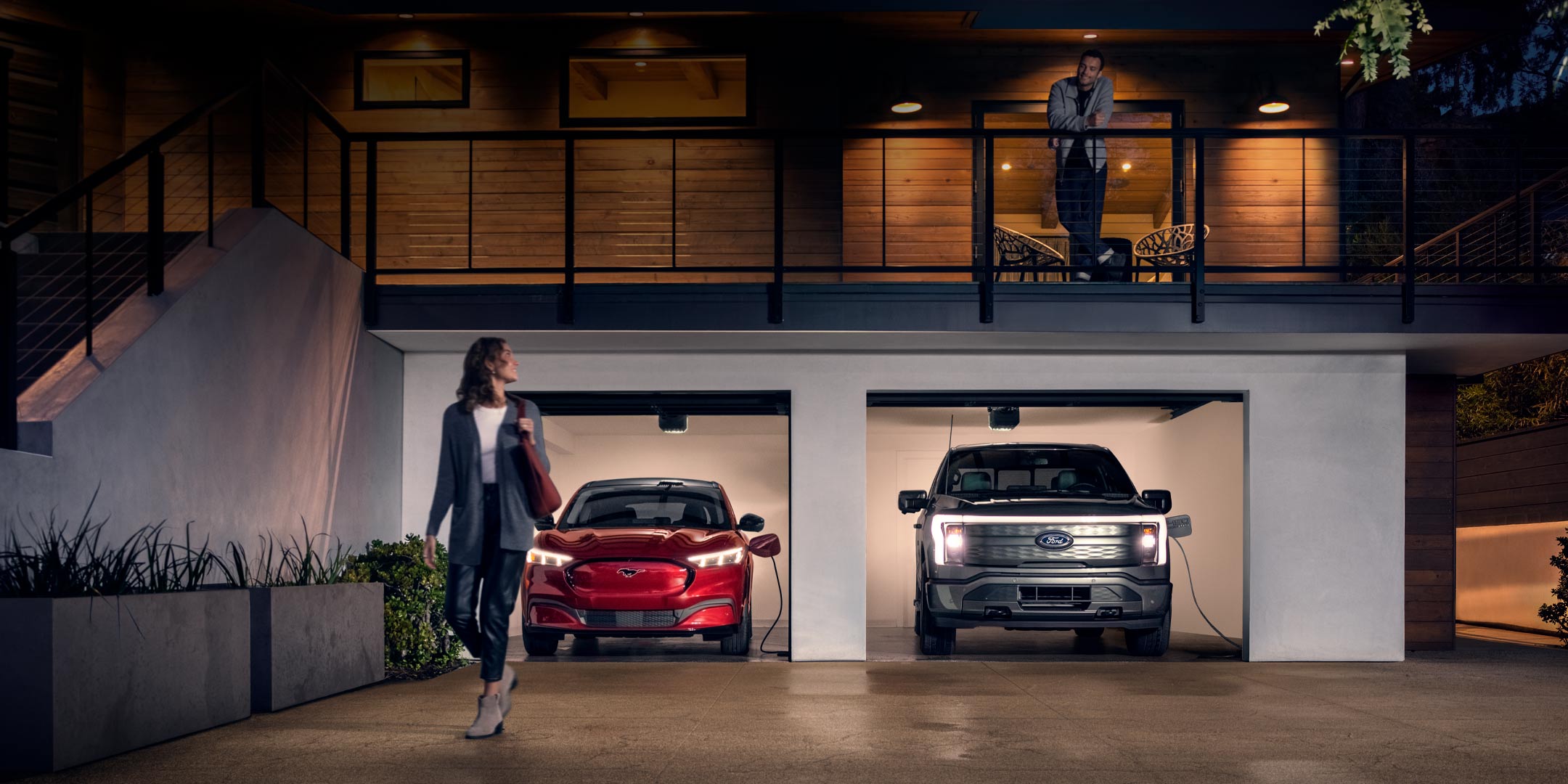 Woman walking out from home garage with a 2024 Mustang® Mach-E and Ford Lightning® truck in plugged-in and charging
