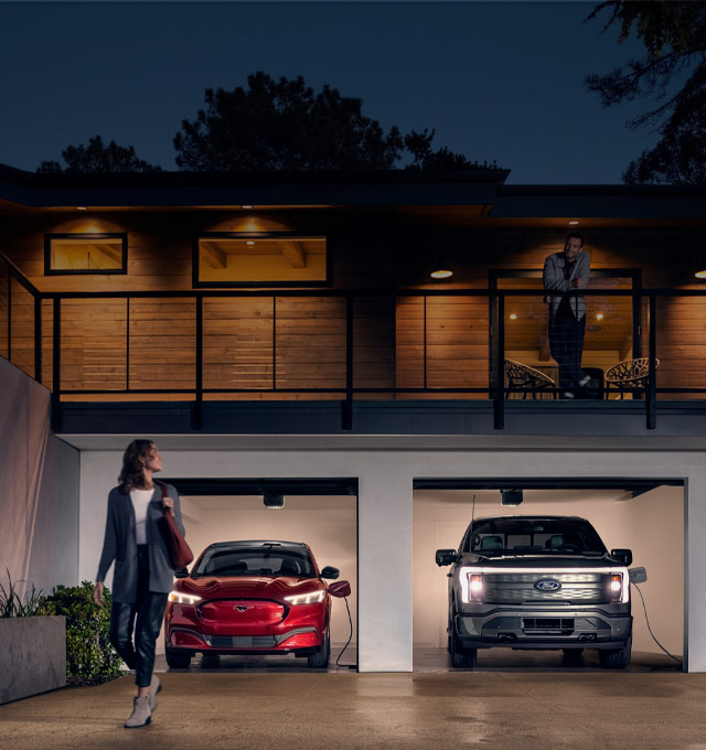 Woman walking out from home garage with a 2024 Mustang® Mach-E and Ford Lightning® truck in plugged-in and charging